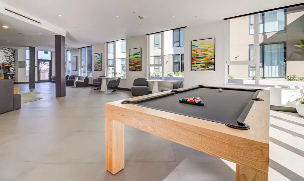 Spacious modern lounge with a pool table in the foreground. Large windows, abstract art, and contemporary furniture create an inviting, relaxed atmosphere.