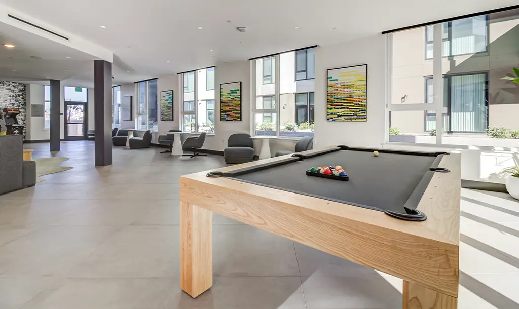 Spacious modern lounge with a pool table in the foreground. Large windows, abstract art, and contemporary furniture create an inviting, relaxed atmosphere.