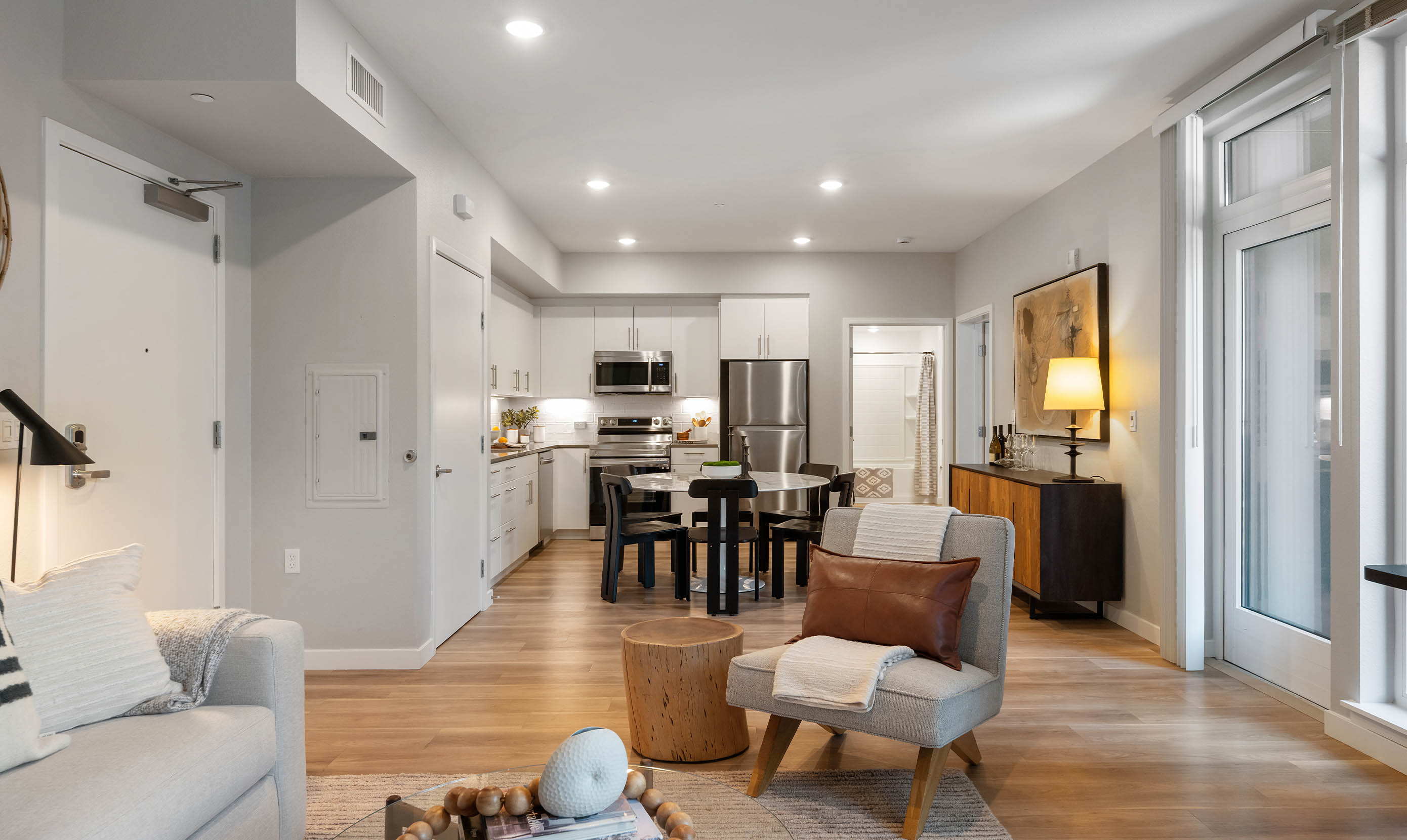 Modern kitchen with white cabinets, stainless steel appliances, and a black table. Chic decor includes a green centerpiece and tan chairs, creating a warm, inviting tone.