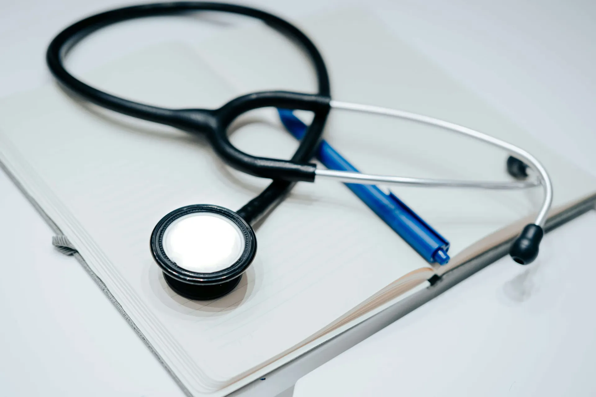 A stethoscope and a blue pen rest on top of a closed laptop on a white surface.