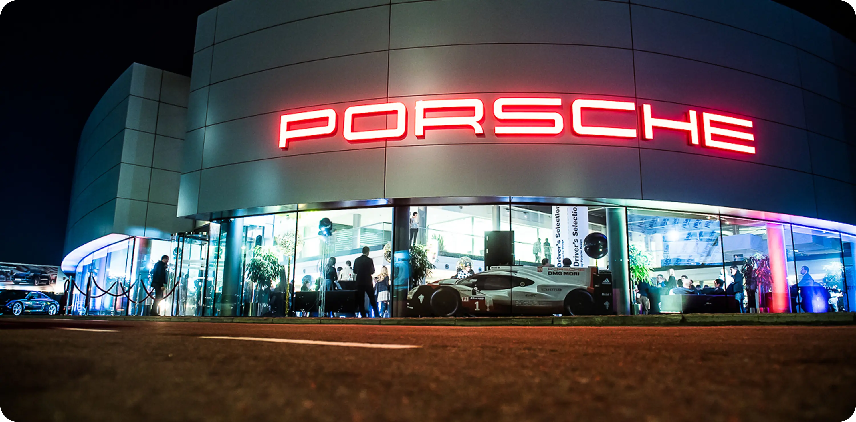 A porsche showroom at night with people standing outside.
