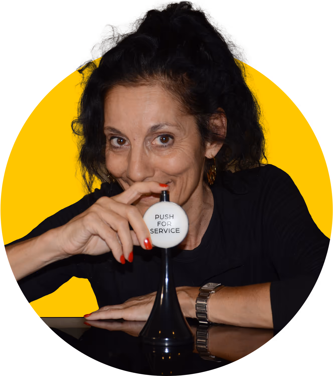 Myriam López sitting at a table, pointing her finger at the button labeled ‘Push for service.’