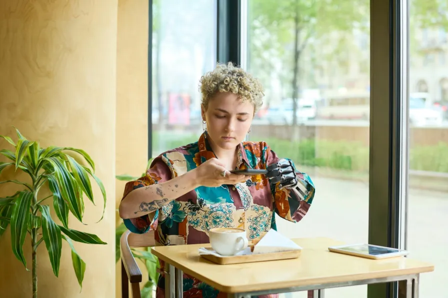 A user with a limb difference navigating a mobile phone at a coffee shop.