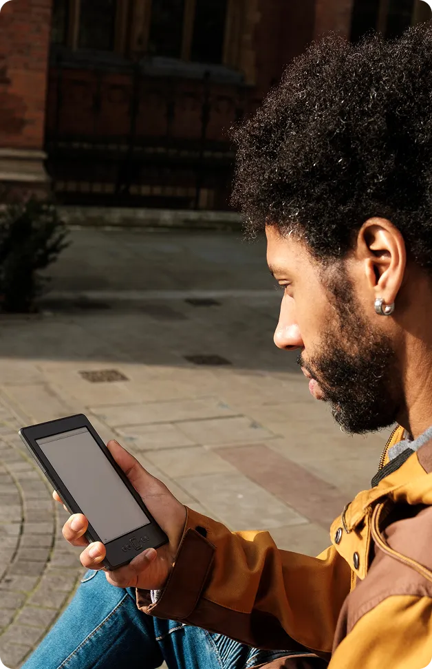 Homme assis en extérieur tenant une liseuse électronique dans sa main droite.