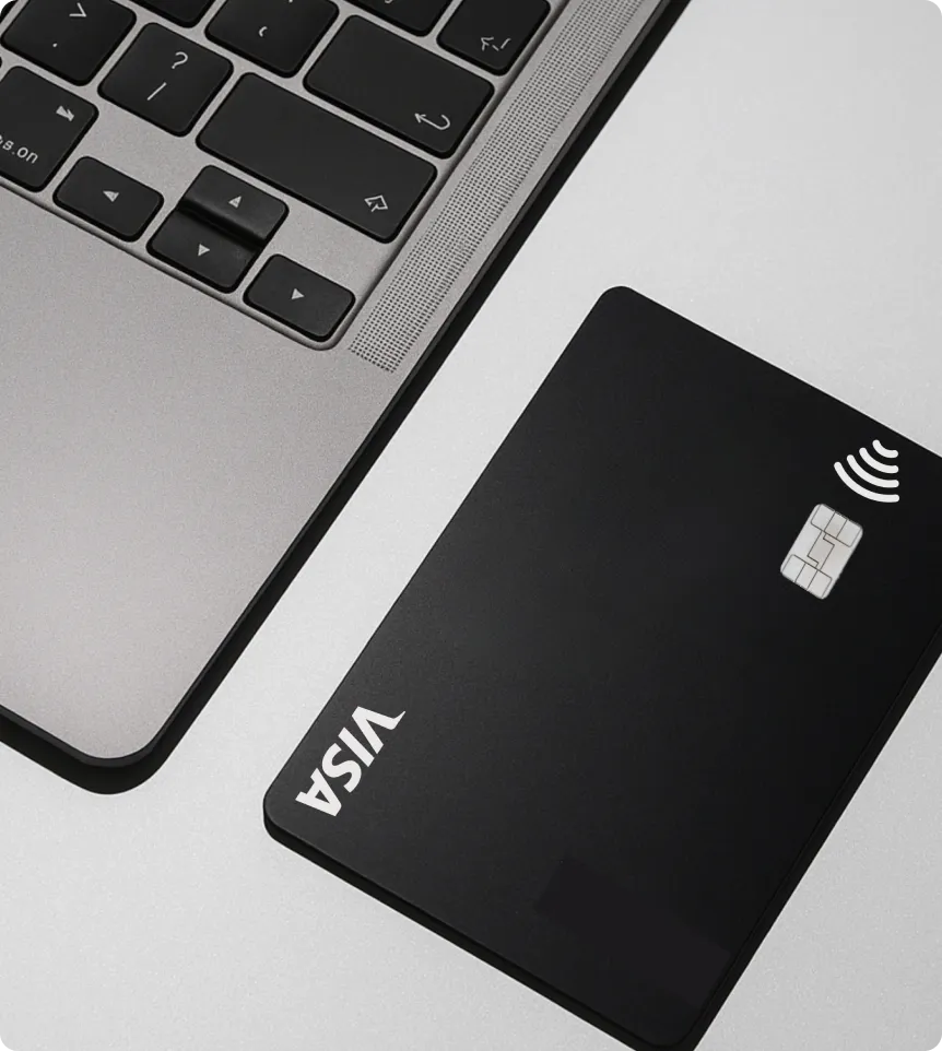 Carte Visa noire avec puce et symbole sans contact à côté d'un clavier d'ordinateur portable gris.