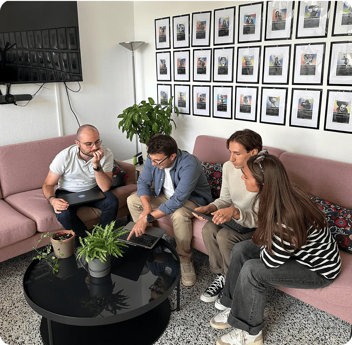 Quatre personnes assises sur des canapés autour d'une table basse noire avec des plantes, discutant et regardant un ordinateur portable.