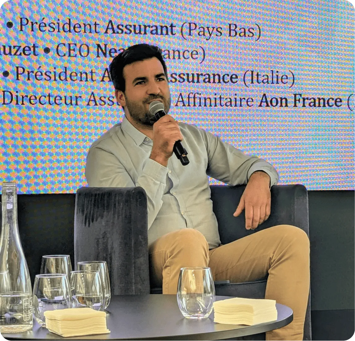 Un homme assis dans un fauteuil tenant un microphone devant un écran avec du texte en français.