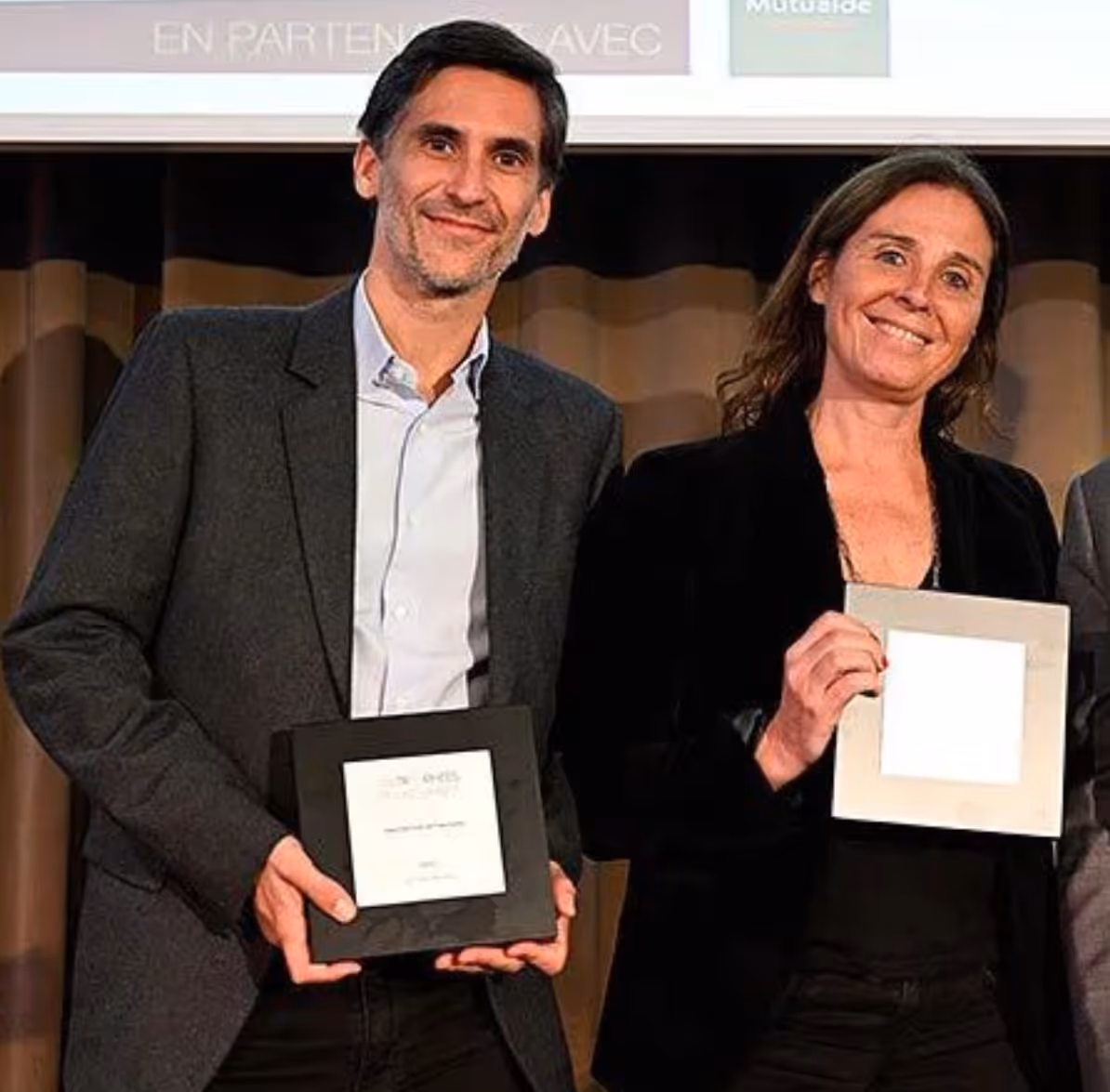 Un homme et une femme souriants tenant chacun un trophée carré lors d’une cérémonie de remise de prix.