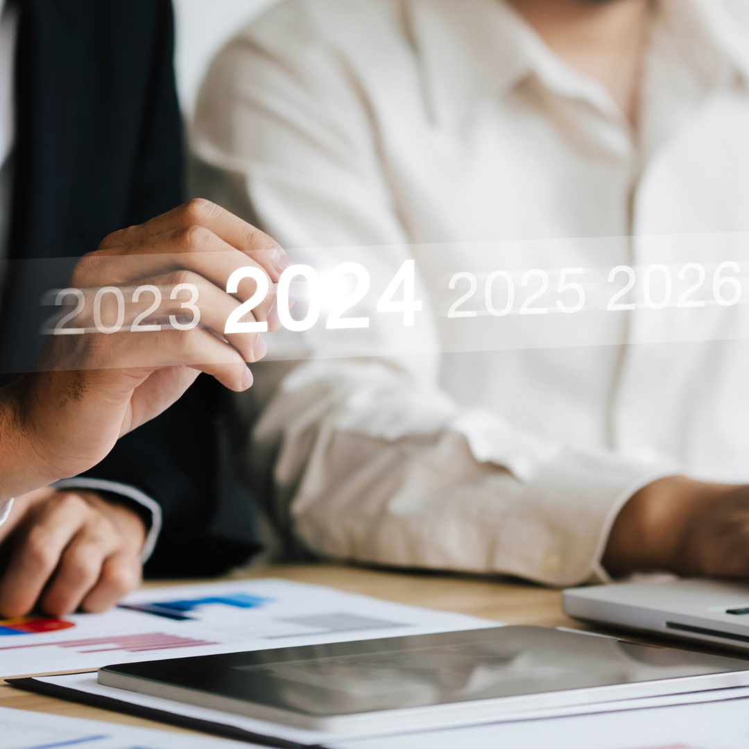  Two people working at a desk with charts and a tablet, while one person points to a glowing digital timeline highlighting the year 2024.