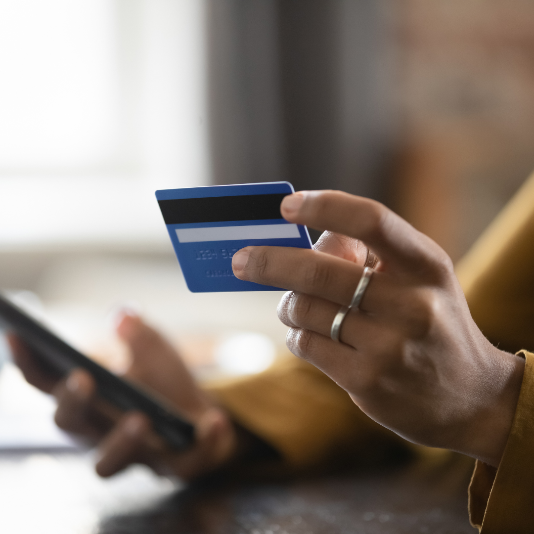 Close-up of a person holding a credit card in one hand and a smartphone in the other while making an online payment.