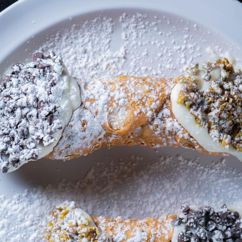 A plate featuring two cannolis dusted with powdered sugar.