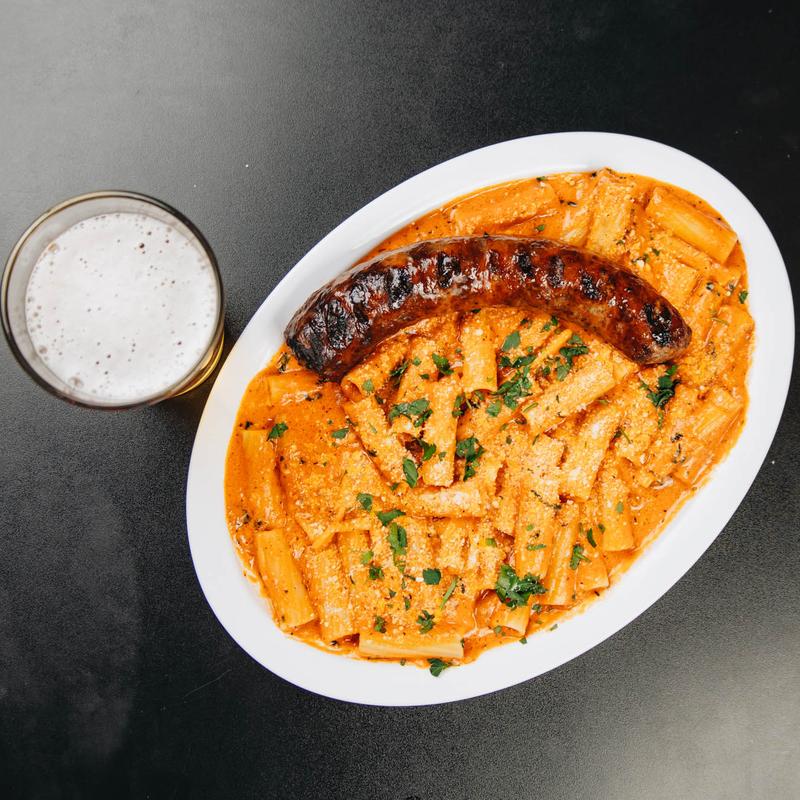 Pasta topped with greens and a grilled sausage.