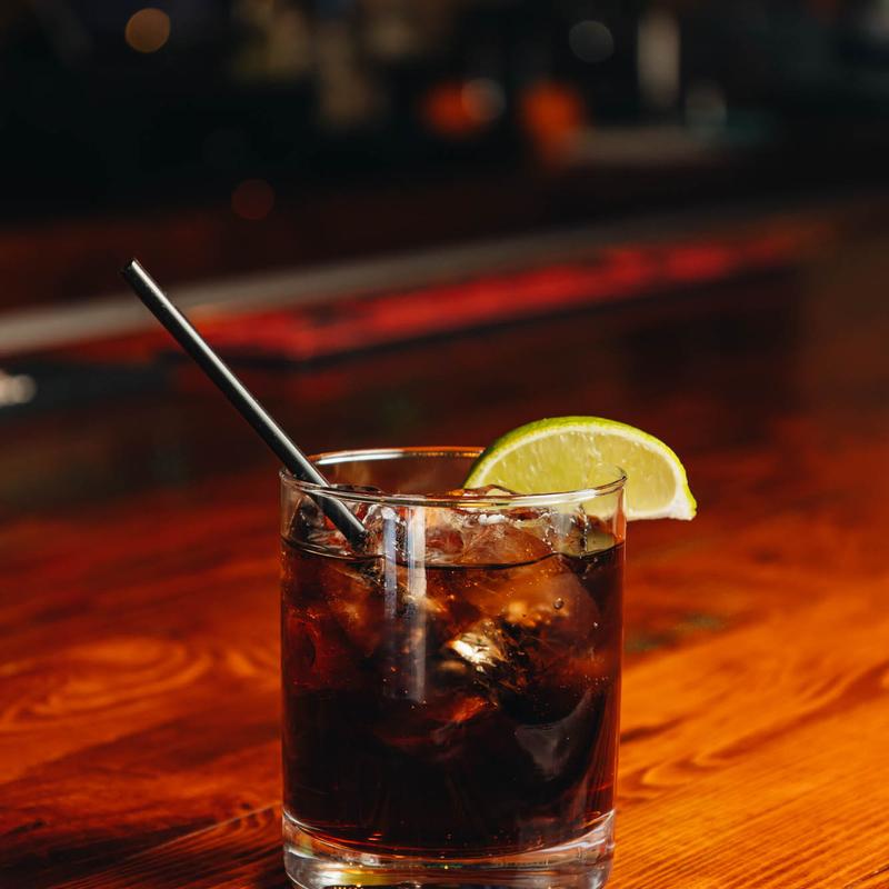 A dark beverage with a straw, set on a rustic wooden table.