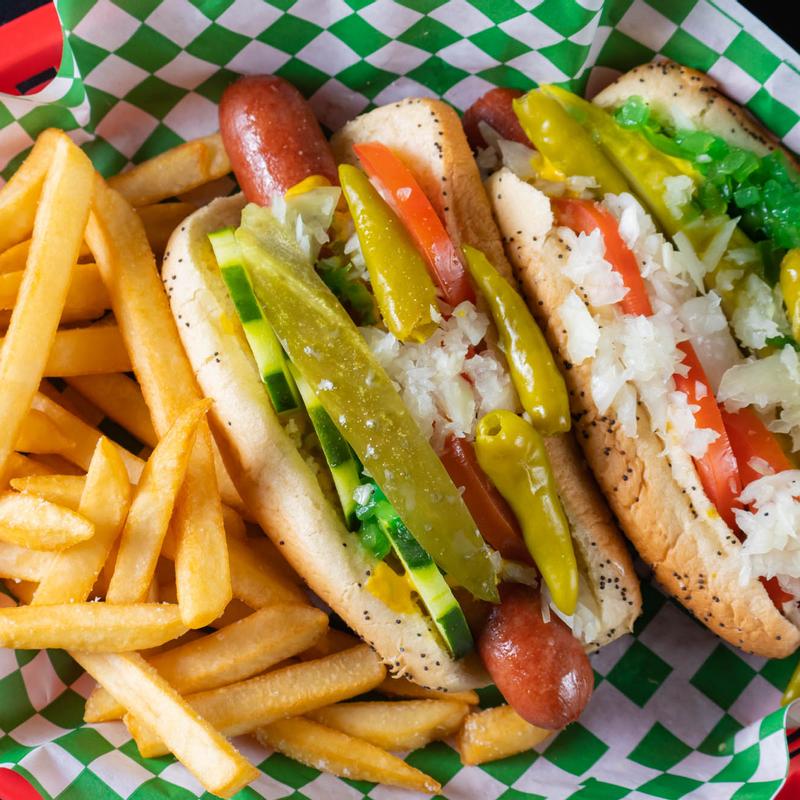 Two hot dogs garnished with vegetables with a side of fries