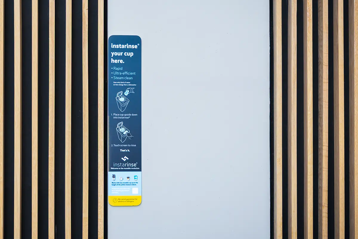 Instarinse signage with instructions for cup cleaning machine promoting reusable cups and sustainable living.
