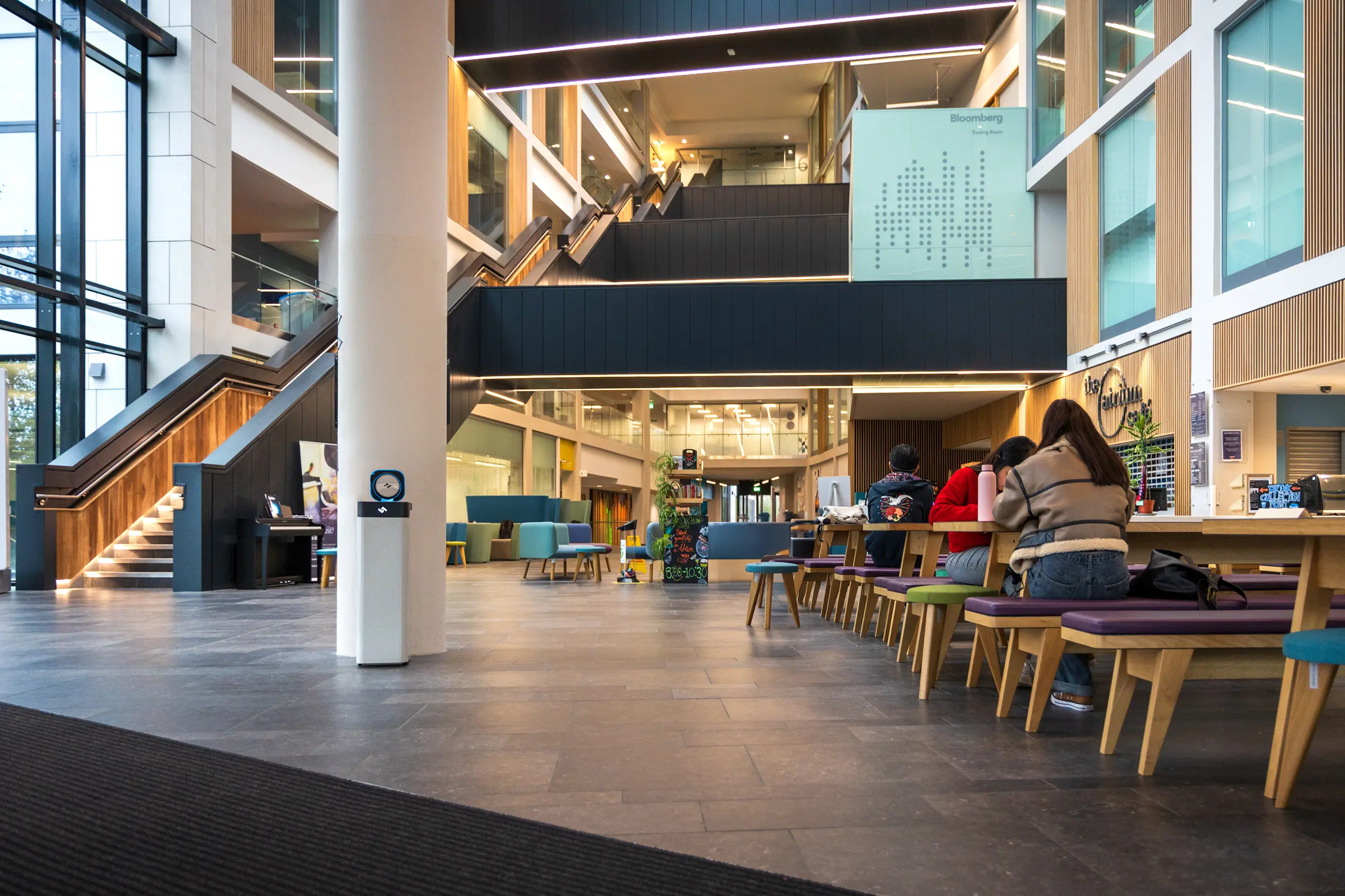Open atrium with seating and an instarinse machine by a column, ideal for campus spaces encouraging reusable cup use.