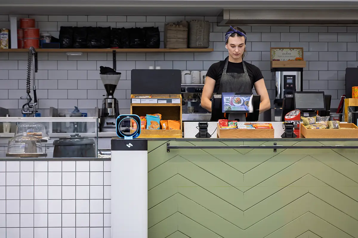 Café counter with barista preparing food and an instarinse cup cleaning machine supporting reusable cups.