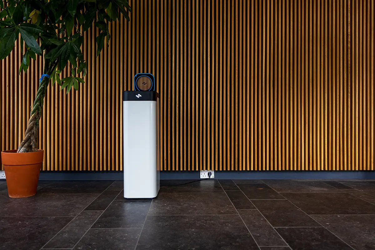 Instarinse cup cleaning machine placed against a wooden slatted wall beside a potted plant in eco-friendly space.