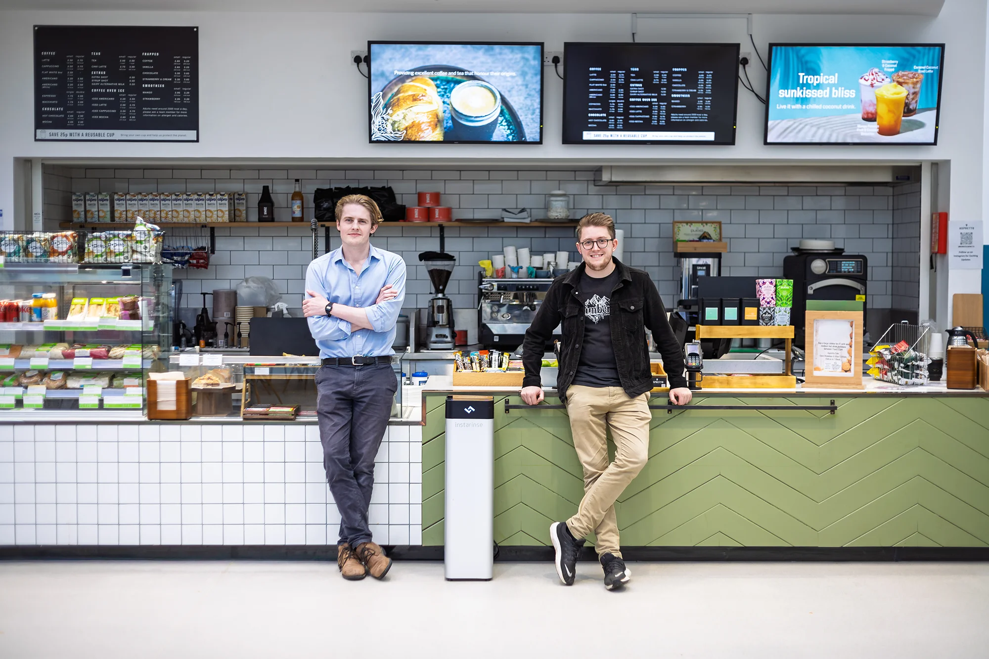 Lava Labs team members standing in a cafe with cup cleaning machine, promoting reusable cups and sustainability.