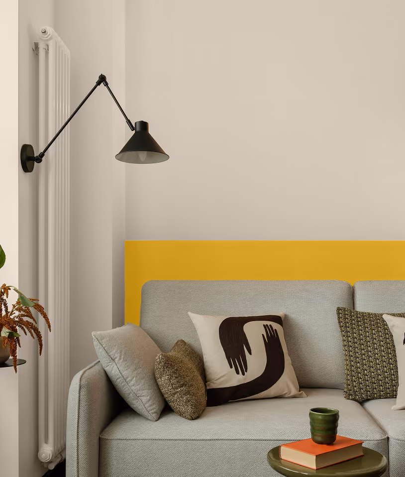 Modern gray sofa with decorative pillows against a beige and yellow accent wall with a black sconce