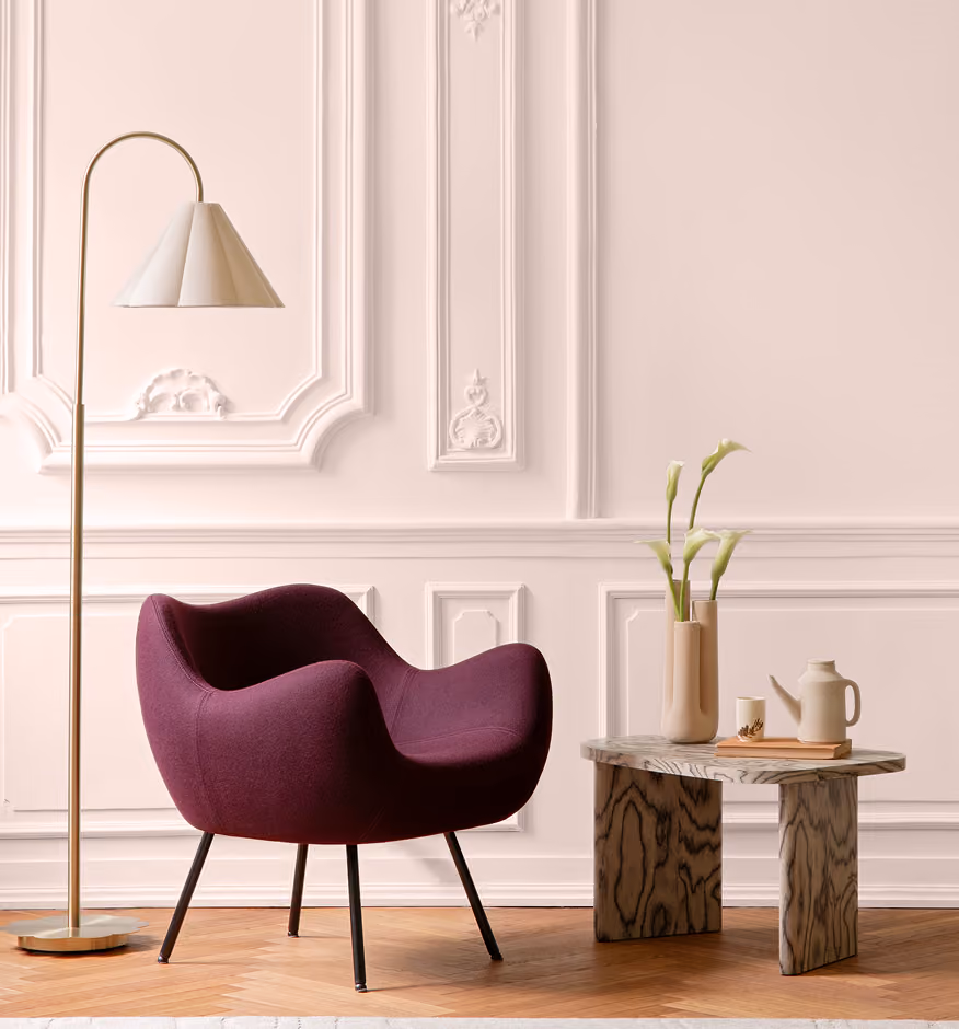 Purple armchair next to a gold floor lamp against a white paneled wall with a small stone table