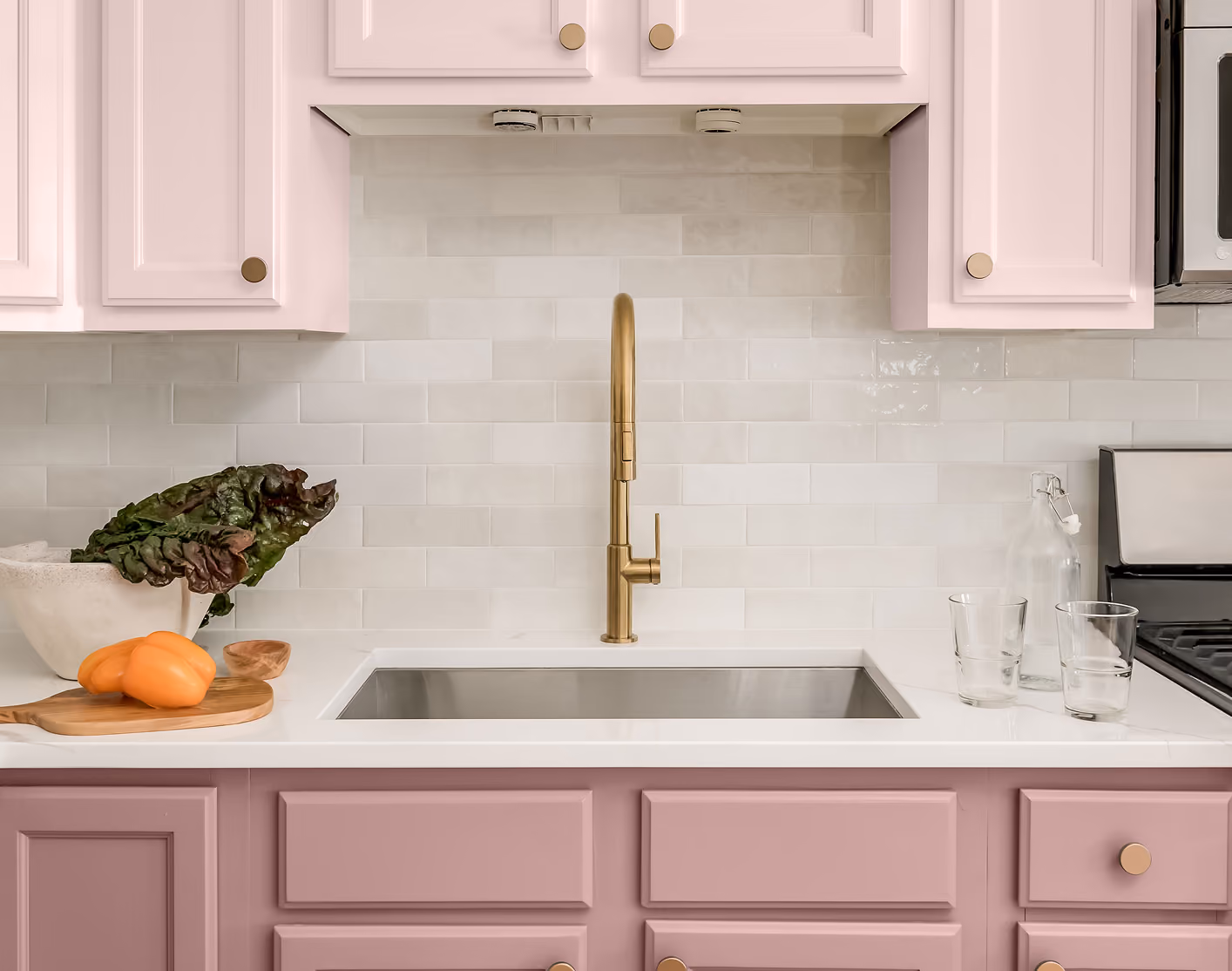 Modern pink kitchen cabinet layout with a white countertop and gold faucet