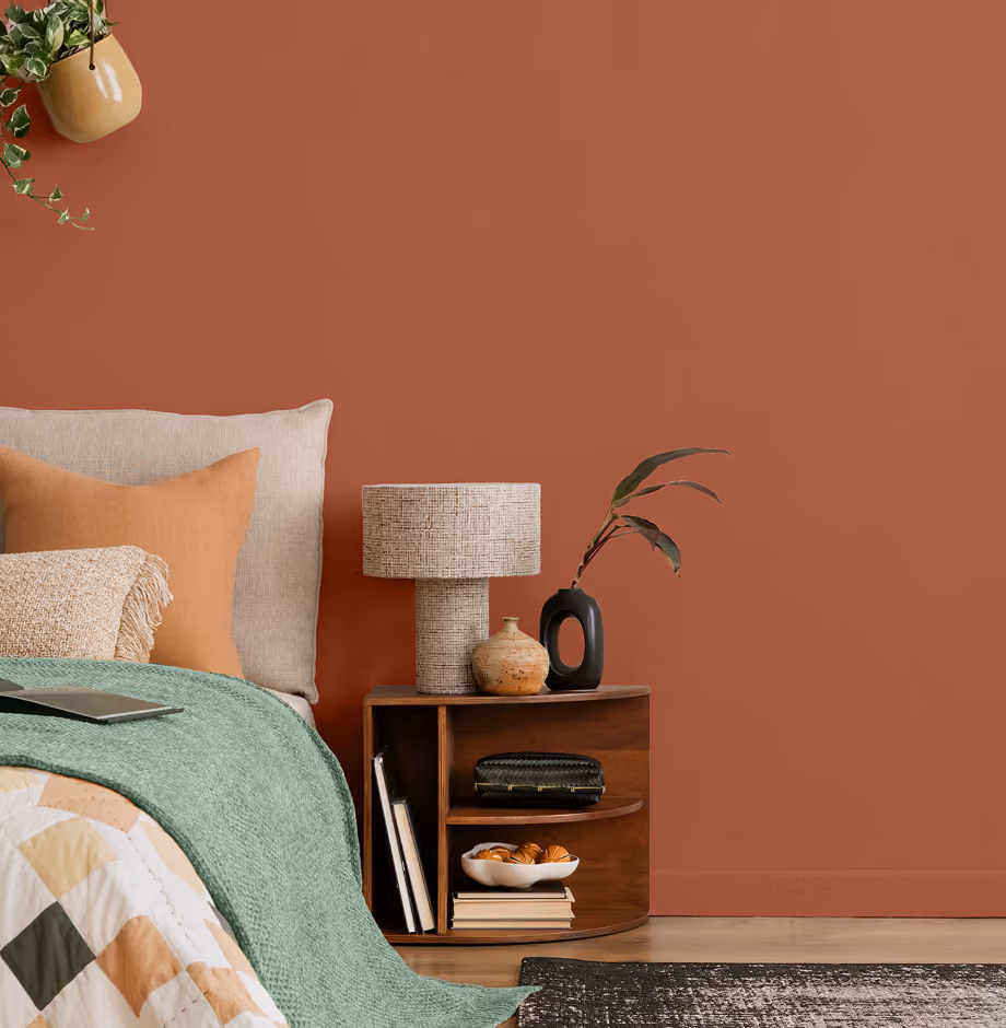 Terracotta accent wall in a bedroom with a wooden nightstand, stone lamp, and green throw blanket