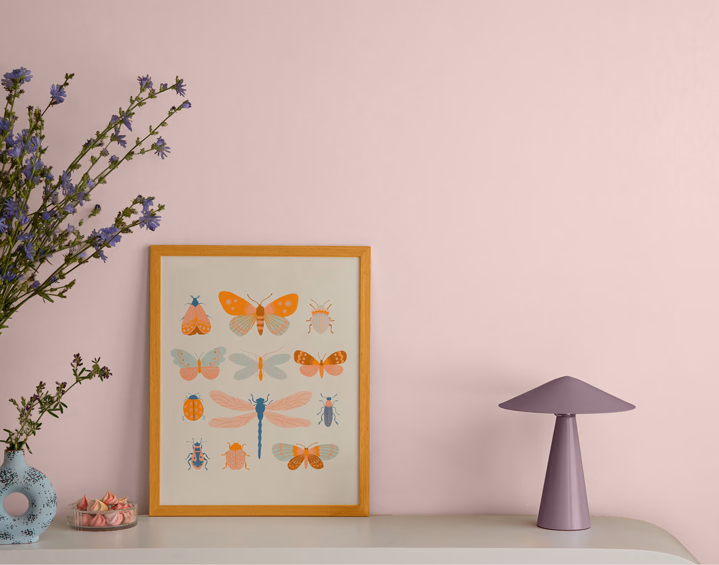 Minimalist pink room with a mushroom lamp, framed insect poster, and flower vase on a table