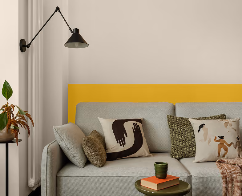 Modern gray sofa with decorative pillows against a beige and yellow accent wall with a black sconce