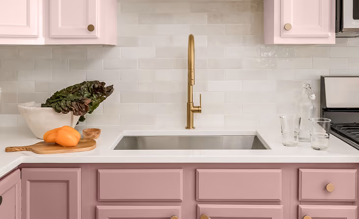 Modern pink kitchen cabinet layout with a white countertop and gold faucet
