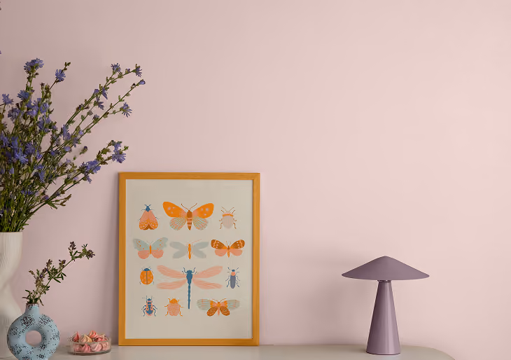 Minimalist pink room with a mushroom lamp, framed insect poster, and flower vase on a table
