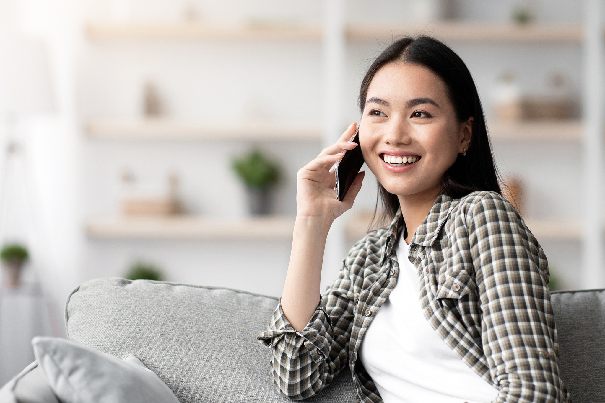 cheerful-asian-lady-sitting-on-sofa-and-talking to a loved one using her IM Telecom wireless service 