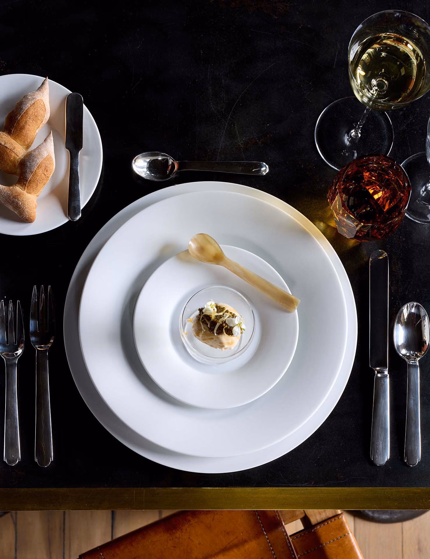 Overhead place setting with bread, wine, and a small appetizer on black table