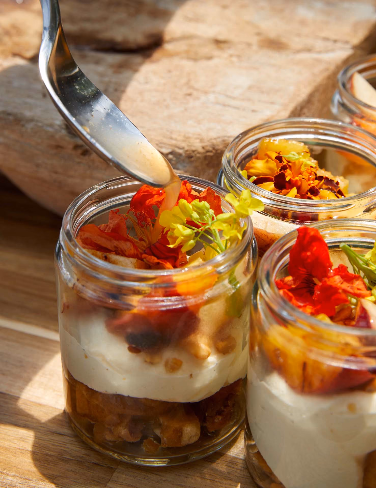 Overhead layered dessert in glass jars topped with orange nasturtium flowers, one being drizzled with sauce