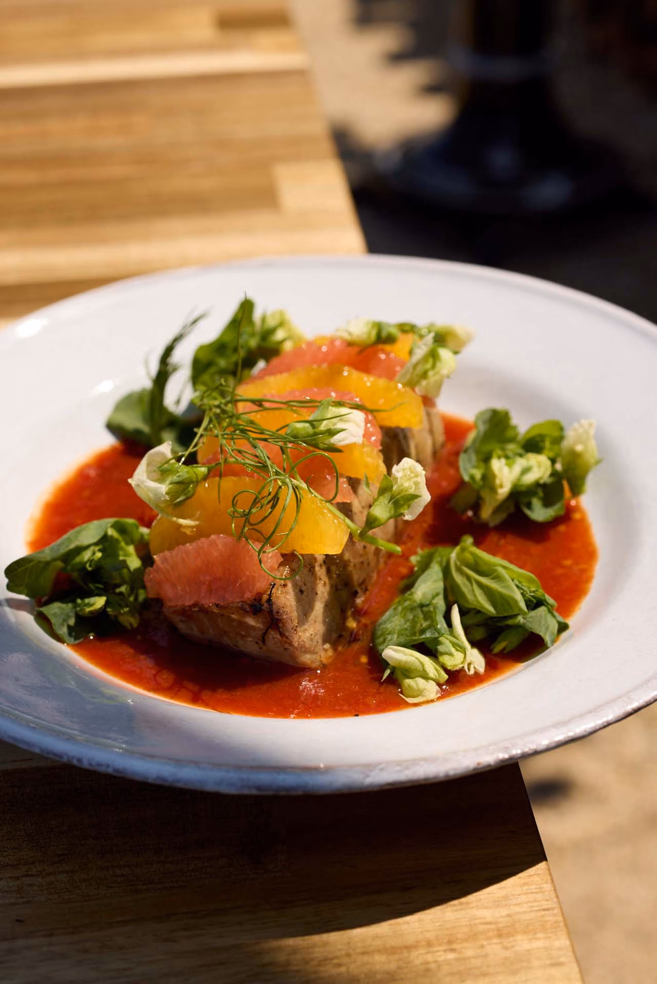 Seared fish fillet with citrus segments and greens in a red gazpacho sauce