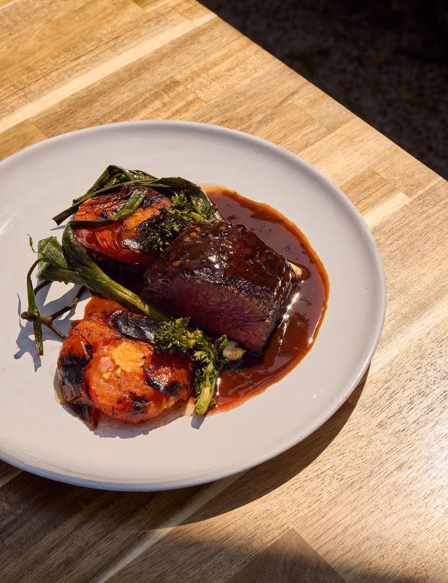 Seared beef fillet with charred tomatoes and scallions in a red wine sauce on a white plate