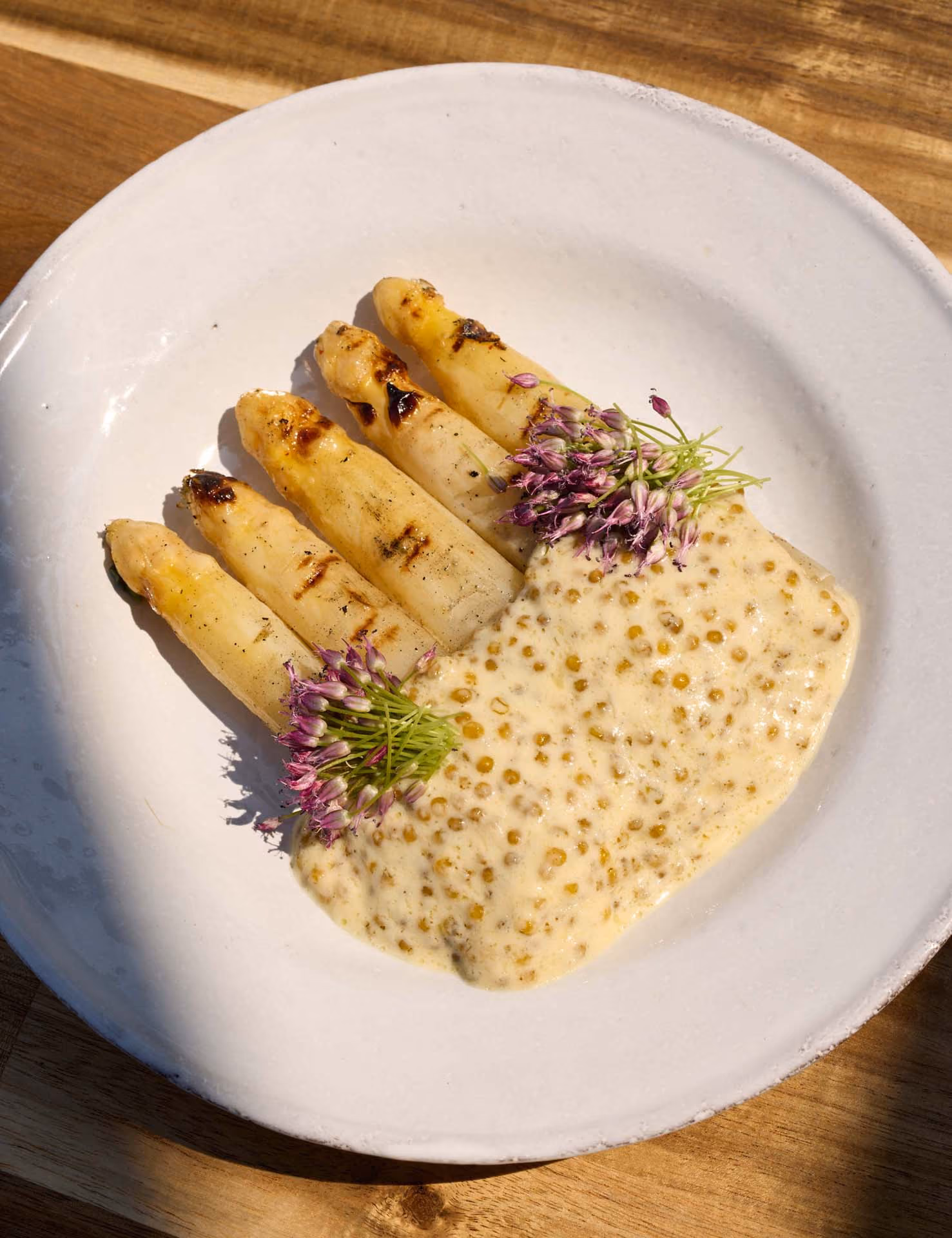 Overhead grilled white asparagus with mustard sauce and chive blossoms on a white plate
