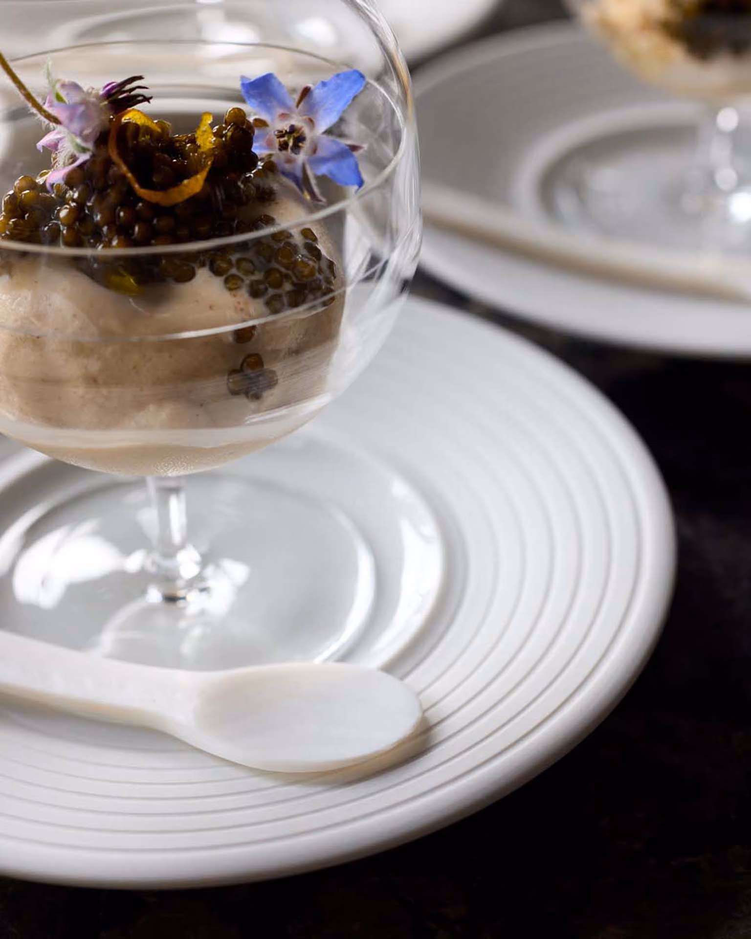 Coupe glass dessert topped with caviar and blue borage flowers on a ribbed white plate