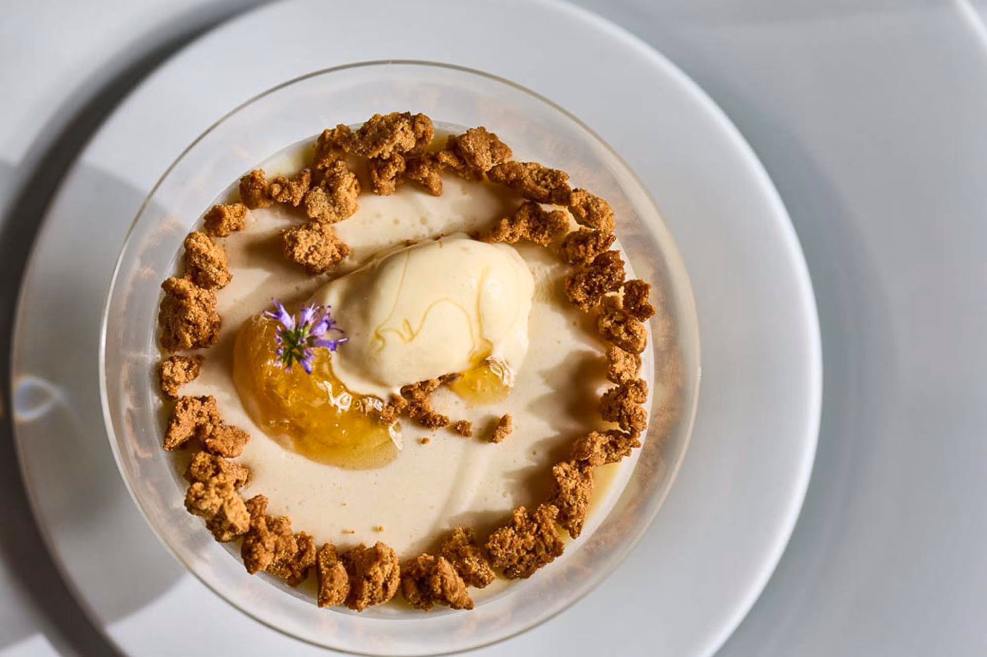 Overhead dessert with a scoop of ice cream, honey, and streusel in a glass bowl