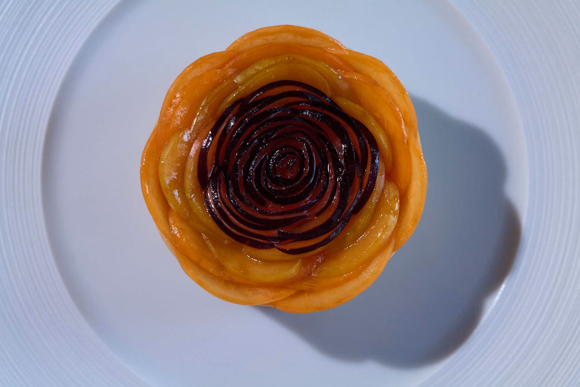 Overhead spiral fruit tart with golden and dark plum slices