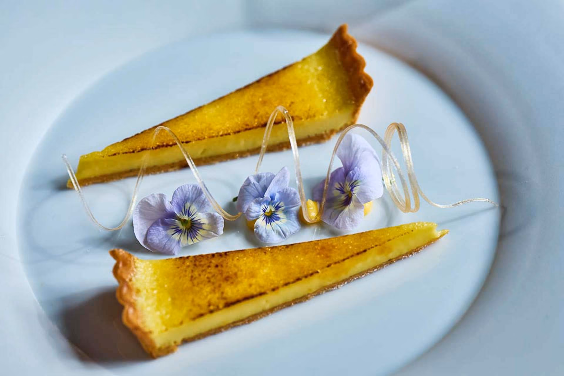 Two slices of lemon tart garnished with pansies and sugar spirals