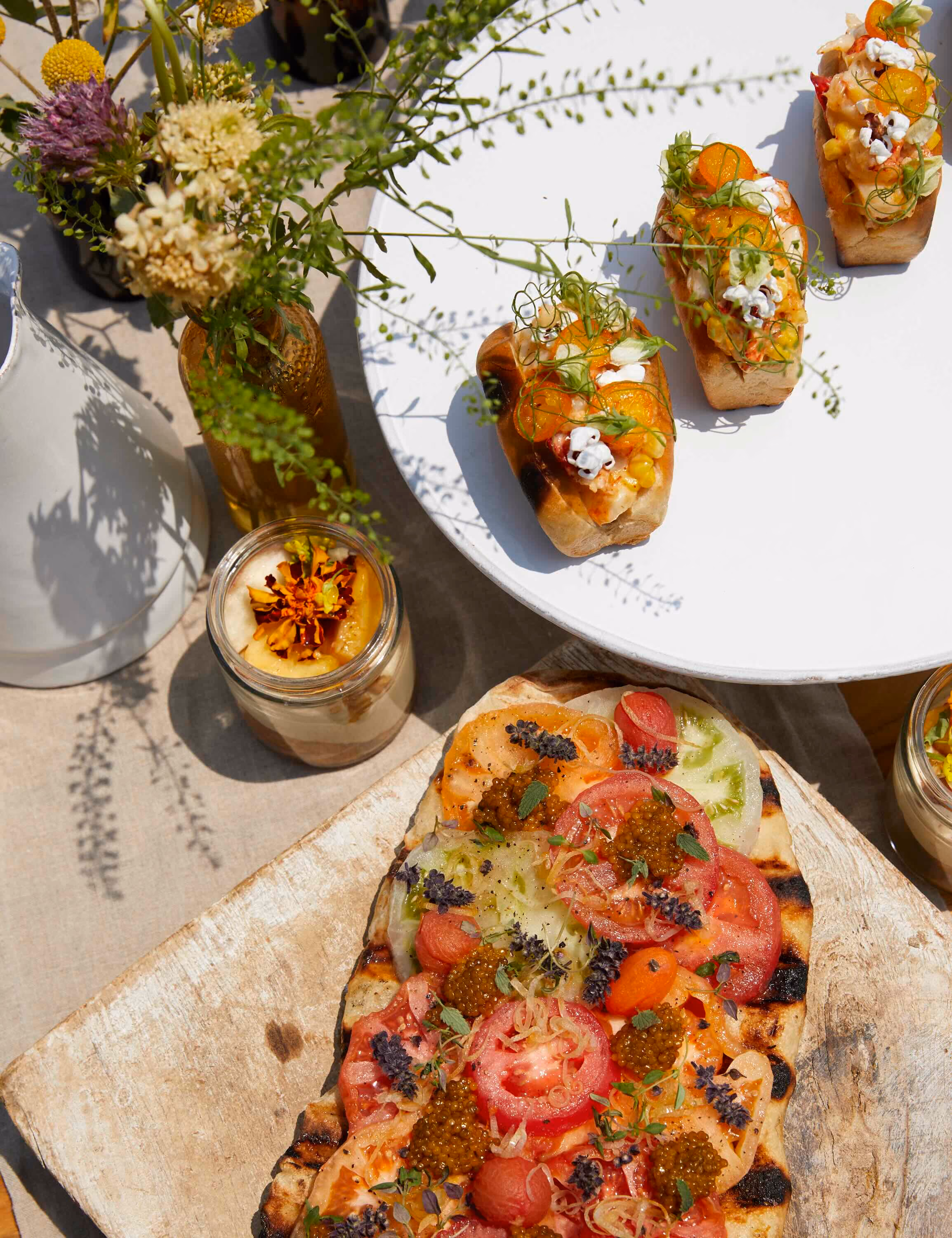Overhead outdoor spread of grilled flatbread with tomatoes and crostini appetizers among flowers