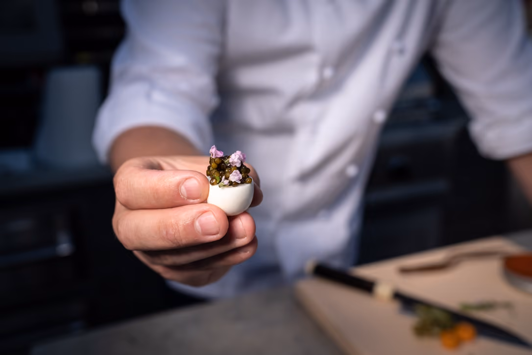Chef holding out a deviled egg topped with caviar and purple flowers
