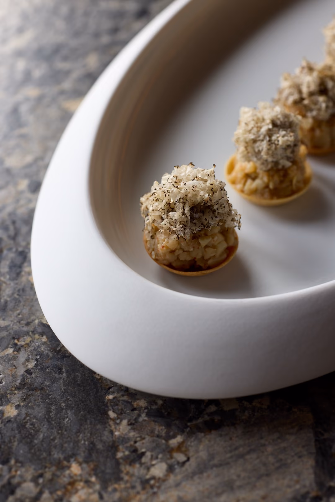 Overhead close-up of herb-crusted seafood canapes on a white curved dish