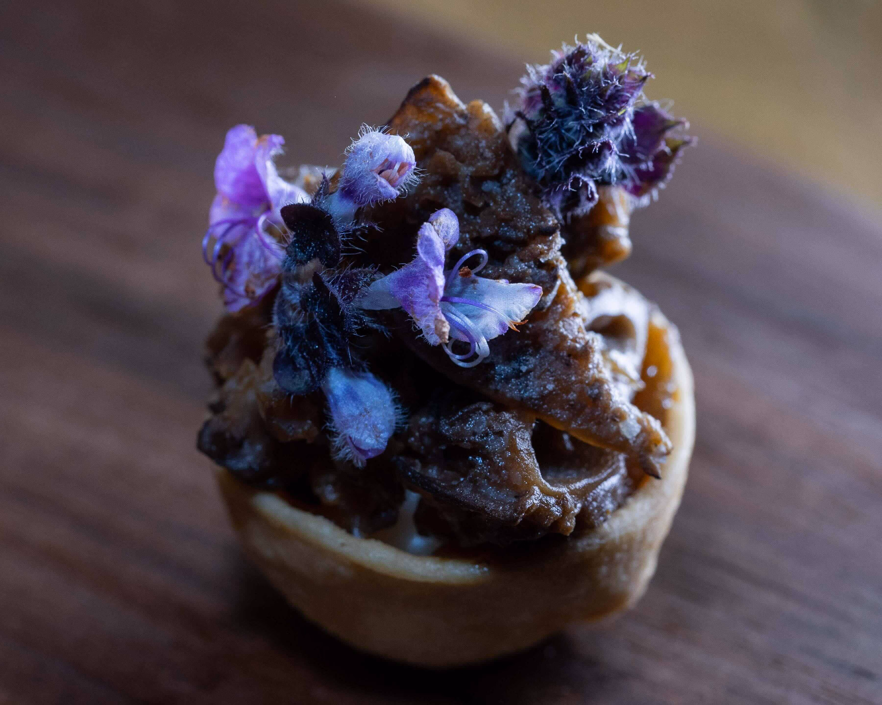 Close-up of a mushroom tartlet topped with purple flowers