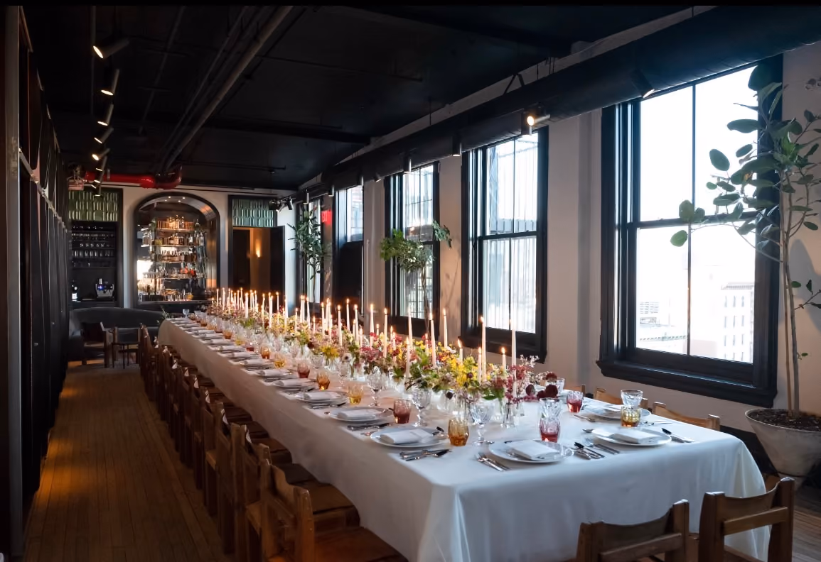 Candlelit long dinner table set in a restaurant with city view windows
