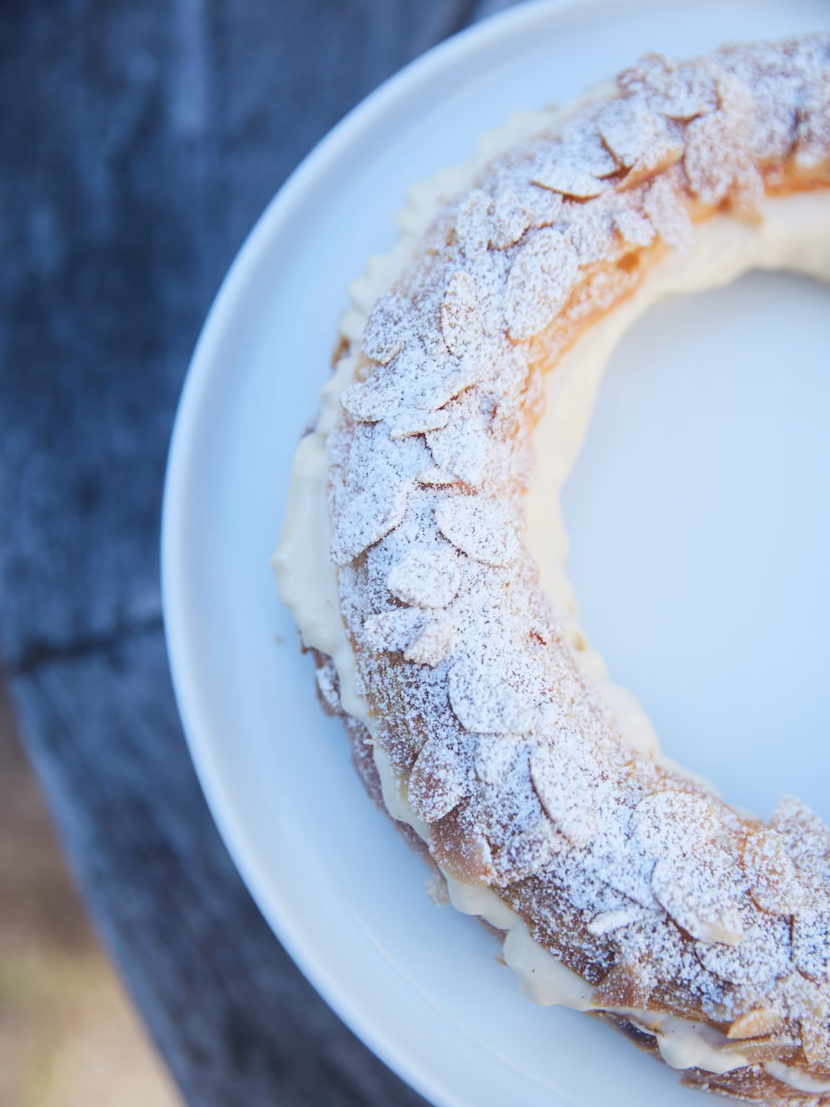 Overhead close-up of a Paris-Brest pastry ring topped with almonds and powdered sugar