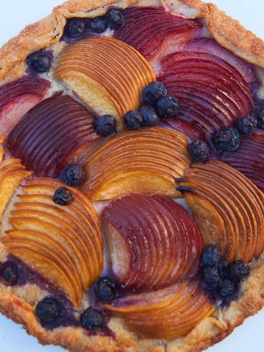 Overhead fruit tart topped with sliced stone fruit and blueberries