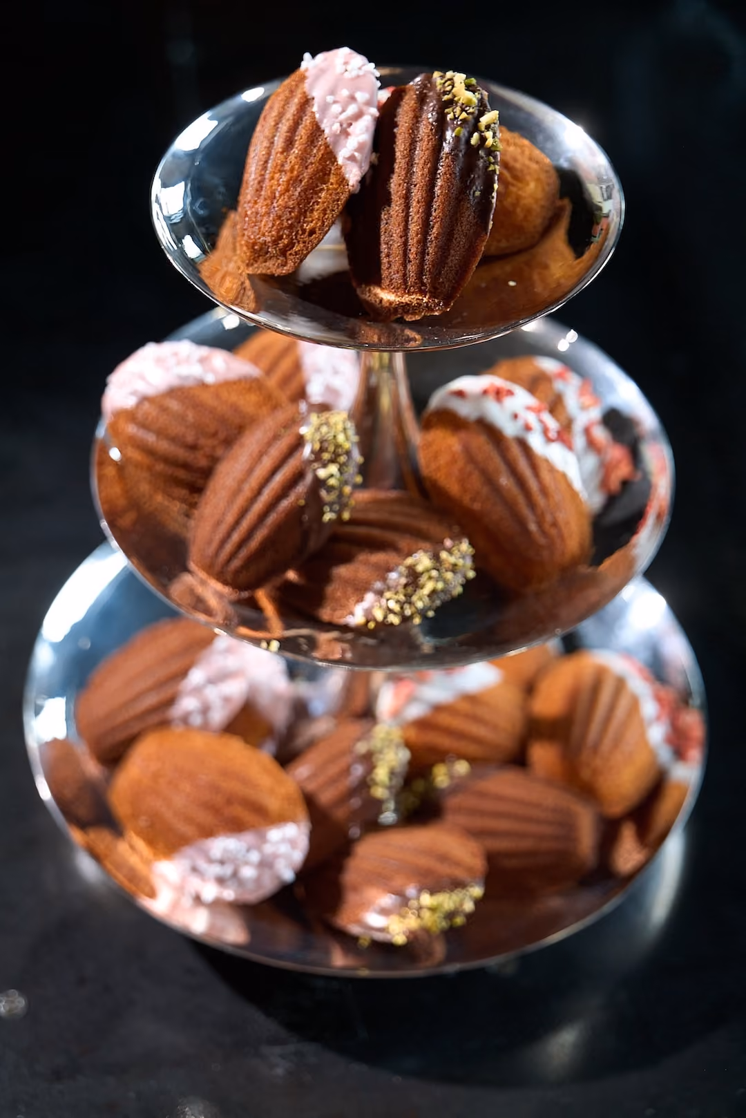 Three-tiered stand of madeleines dipped in chocolate and pink glaze with pistachio