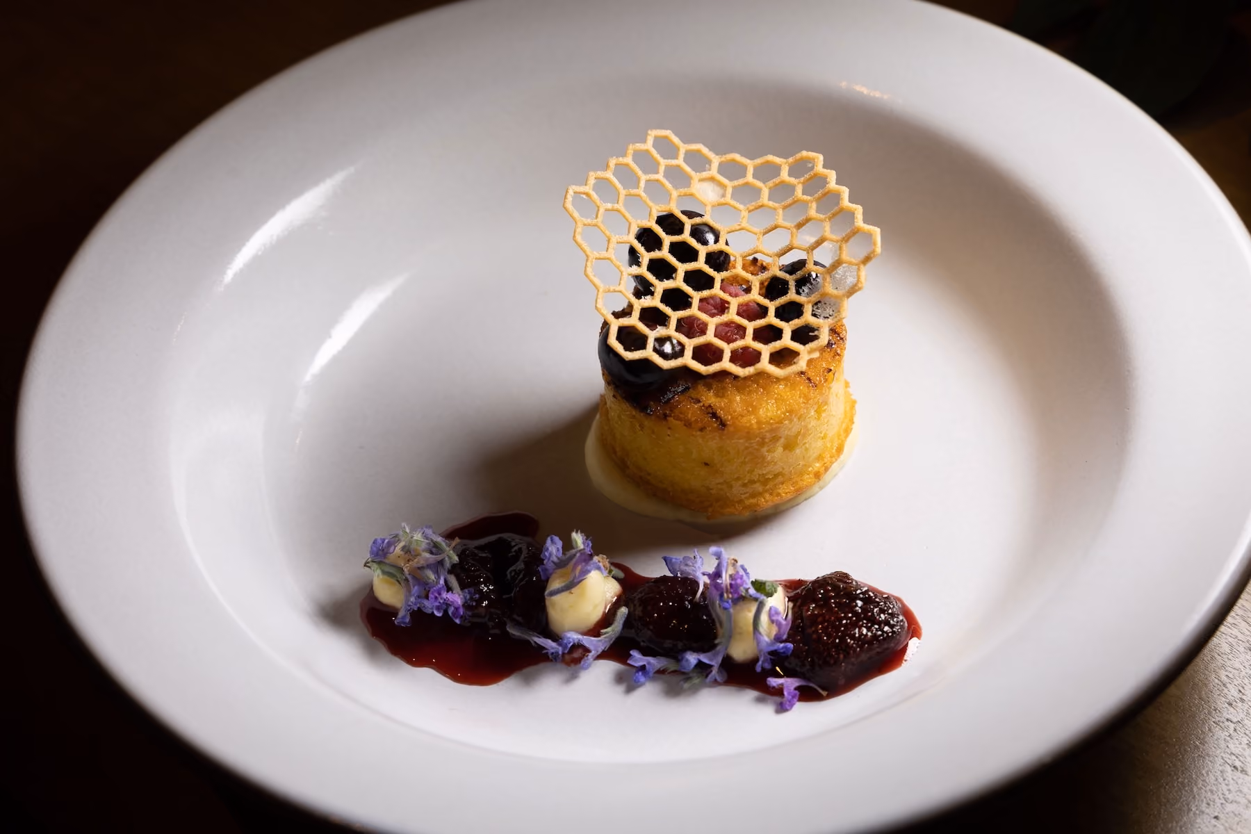 Individual dessert with a honeycomb tuile and blackberries, plated with fig compote and purple flowers